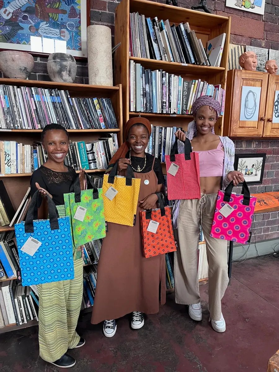 Imbali makers holding up handmade Shwe Shwe bags